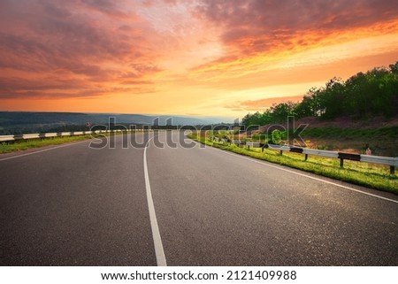 Curving asphalt road under a dramatic sunset sky