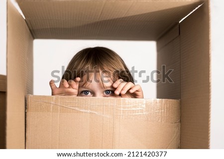 Excited little boy jumping inside a huge cardboard box. He is playing and looking out of a box. Kid is happy about moving into a new home. Royalty-Free Stock Photo #2121420377