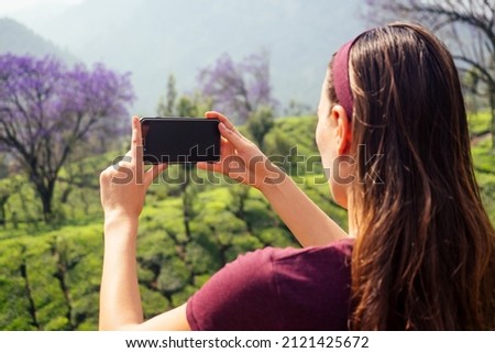 young girl enjoying a good morning taking picture photo on camera of phone in tea plantations in India Munnar Kerala