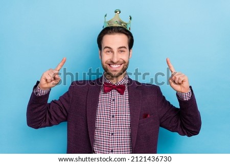 Photo of young cheerful handsome man indicate fingers golden crown brand isolated over blue color background