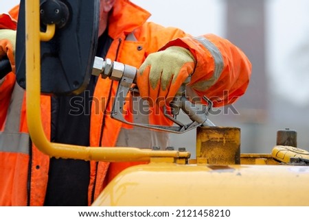 Construction worker in safety gloovs filling excavator with diesel fuel on construction site Royalty-Free Stock Photo #2121458210