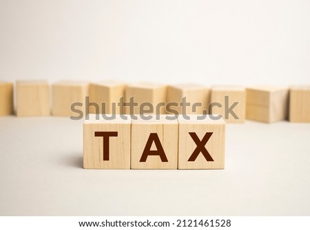 Three wooden cubes with the letters TAX on the bright surface of a gray table. the inscription on the cubes is reflected from the surface of the table. business concept