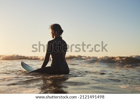 She's as calm as the ocean. Rearview shot of a young woman surfing in the ocean.