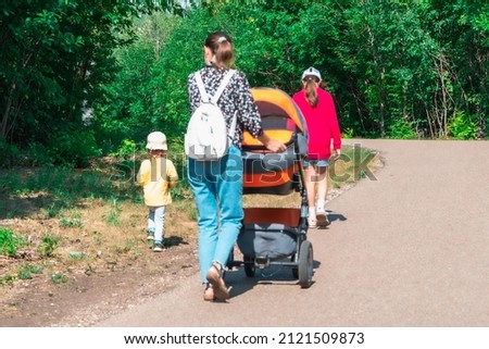 Family, children and mother with a stroller are walking in the park. Blurred.