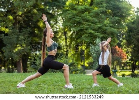Mom with little daughter practice yoga asana warrior 1 pose in the park. Mom trainer, spending time together, healthy family concept