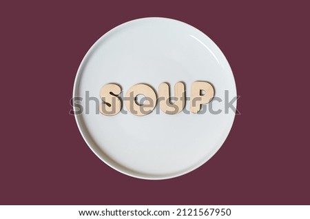 The word Soup made of wooden letters on a round white plate on a colored background