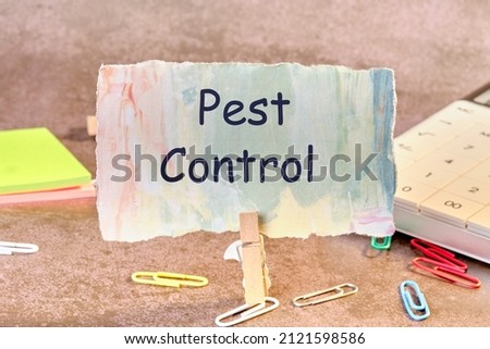 PEST CONTROL phrase written on paper next to scattered paper clips, calculator, adhesive paper.