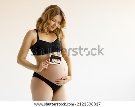 Prenatal ultrasound screening. Beauty pregnant holding sonogram picture of unborn baby inside her big belly. Happy expectant mom showing fetus usi scan image to camera