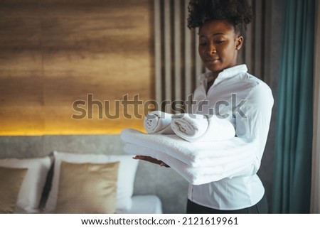 Change of towels in the hotel room. A uniformed maid is cleaning up the hotel room. Towels in the hands of the maid. The concept of the hotel business. Photos in the interior.