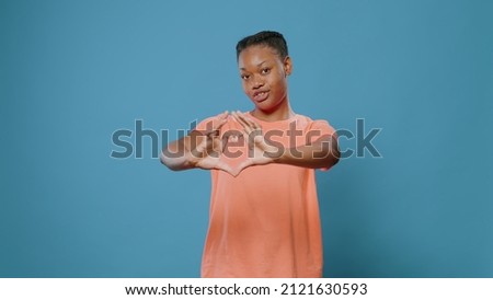 Young woman doing heart shape symbol with hands in studio. Affectionate person showing love sign and romantic gesture, expressing feelings and affection, standing over isolated background.