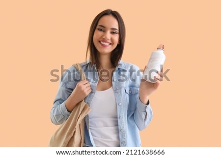 Young woman with eco bag and bottle on beige background Royalty-Free Stock Photo #2121638666