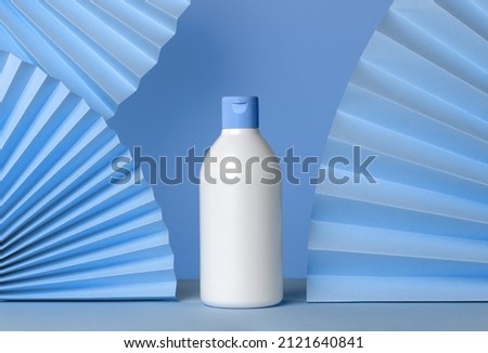 Creative composition with white bottle and textured blue paper fans. Mockup for products with copy space. Natural organic spa concept for face and body care. 