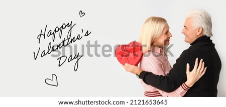 Happy mature couple with gift on light background. Happy Valentine's Day celebration