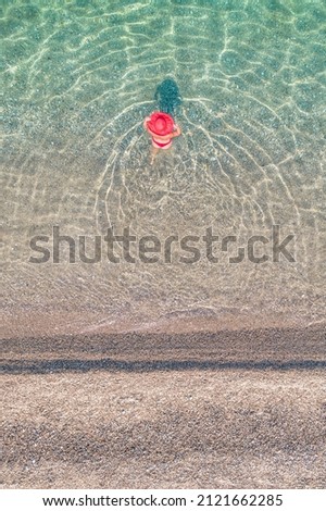 Top, aerial view. Young beautiful woman in a red hat and bikini walking, swimming, sunbathe in sea water on the sand beach. Drone, copter photo. Summer vacation. View from above. 