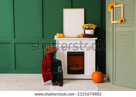 Interior of room with beautiful Chrysanthemum flowers and blank photo frame on fireplace near color wall