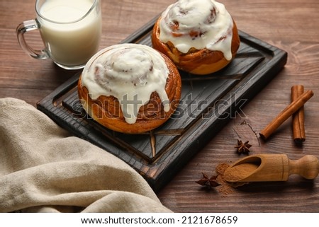 Board of tasty cinnamon rolls with cream on wooden background