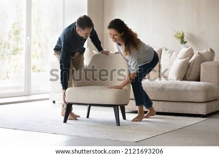 Happy loving couple placing modern furniture in new apartment, smiling man and woman carrying armchair, moving into new home, decorating living room together, relocation and interior design concept Royalty-Free Stock Photo #2121693206