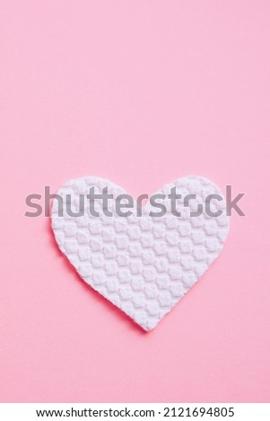 White fabric heart on pastel pink table.