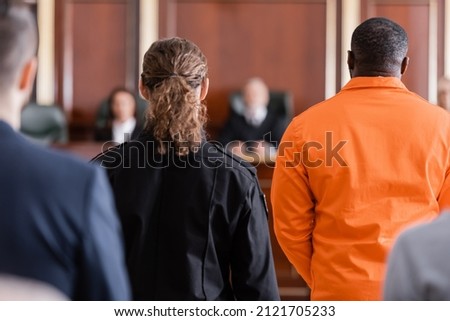 back view of accused african american man near guard and blurred jurors in courtroom Royalty-Free Stock Photo #2121705233