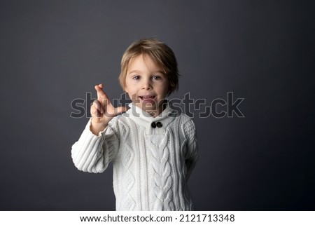 Cute little toddler boy, showing WISH FOR LUCK gesture in sign language on gray background, isolated image, child showing hand sings