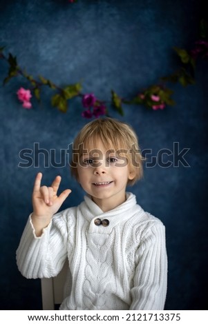 Cute little toddler boy, showing I LOVE YOU gesture in sign language on blue background, isolated image, child showing hand sings
