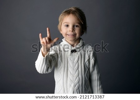 Cute little toddler boy, showing I LOVE YOU gesture in sign language on gray background, isolated image, child showing hand sings