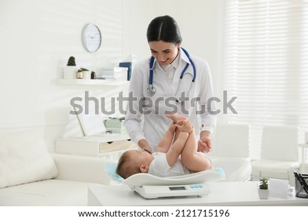Young pediatrician weighting cute little baby in clinic Royalty-Free Stock Photo #2121715196