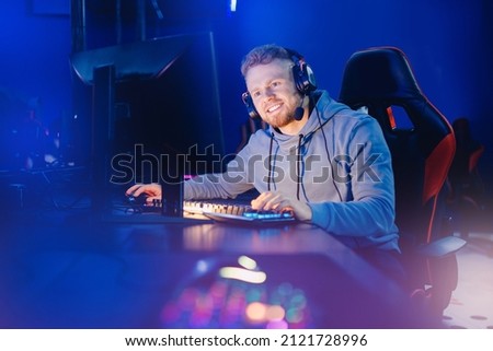 Streamer young man on chair in game studio. Gamer playing action video tournament online in dark room neon color.