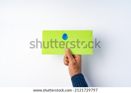 Male hand holding closed envelope above the white surface, top view