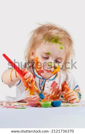 The child draws attentively. Face, hands and clothes smeared with paint