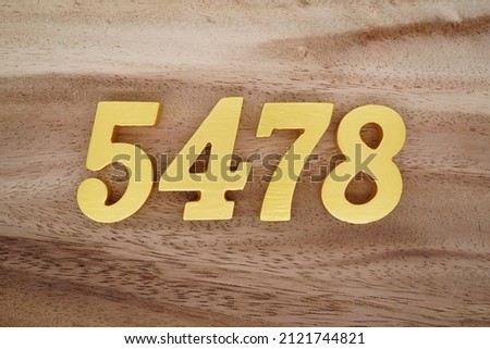 Wooden Arabic numerals 5478 painted in gold on a dark brown and white patterned plank background.