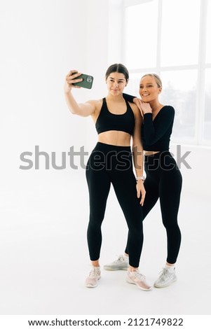 Cheerful fitness women sitting together for a selfie at the gym. Fitness woman taking a selfie with gym trainer using a mobile phone.