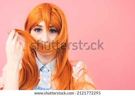 stylish caucasian costume player teenager playing with her ginger hair making moustache - pink background. High quality photo