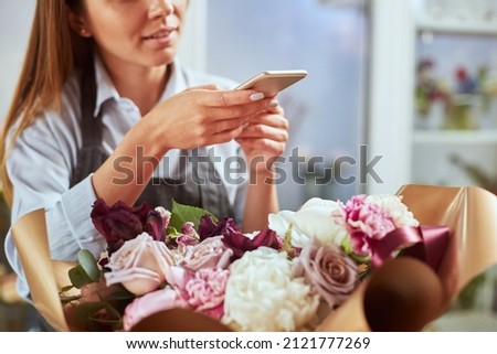 Close up portrait of female florist taking picture of freshly made bouquet on smart phone, creating content for social media. Small local business, self employed, blogger concept