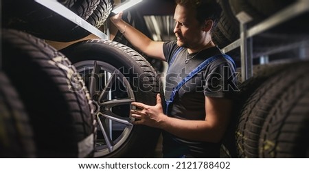 Hardworking experienced worker holding tire and he wants to change it In the tire store. Selective focus on tire. Royalty-Free Stock Photo #2121788402