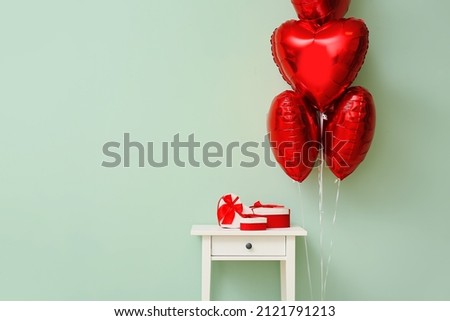 Beautiful heart-shaped balloons for Valentine's Day celebration and table near color wall