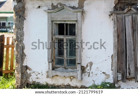 An old, abandoned house with windows in a rustic landscape. A collapsed building with worn paint in a small settlement. Selective focus. Retro and vintage. A copy of the space. Front view. 