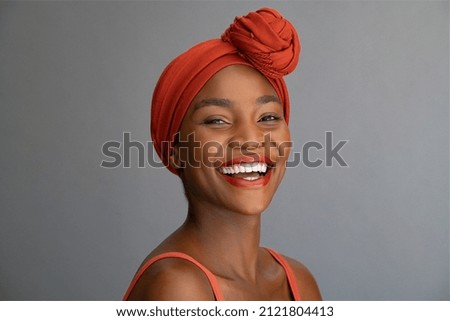 Portrait of cheerful african mature woman with headscarf against grey wall. Middle aged black woman laughing, copy space. Happy smiling black lady wearing traditional african scarf and looking at came Royalty-Free Stock Photo #2121804413