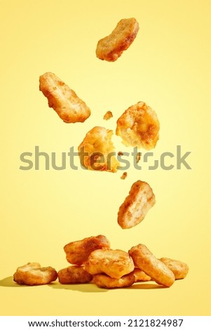 Flying chicken nuggets, one broken in half on yellow background Royalty-Free Stock Photo #2121824987