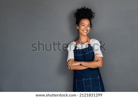 Young black woman wearing apron isolated on grey background with copy space. Portrait of successful african american woman with crossed arms on gray wall. Smiling black waitress looking at camera. Royalty-Free Stock Photo #2121831299