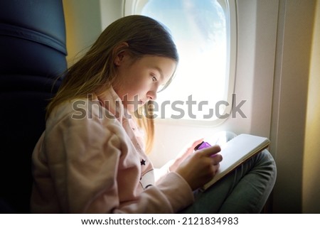 Adorable young girl traveling by an airplane. Child sitting by aircraft window and drawing a picture with colorful pencils. Traveling abroad with kids.