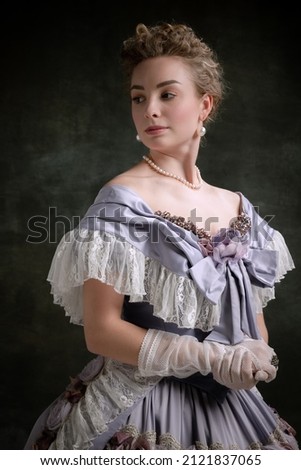 Noble lady. Vintage portrait of young adorable girl in image of medieval royal person in renaissance style dress isolated on dark background. Comparison of eras, beauty, history, art, creativity. Royalty-Free Stock Photo #2121837065