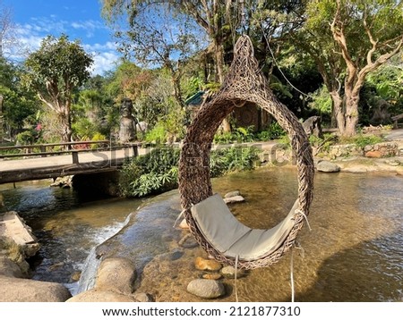 There is a wooden swing in the back with a waterfall and various trees.