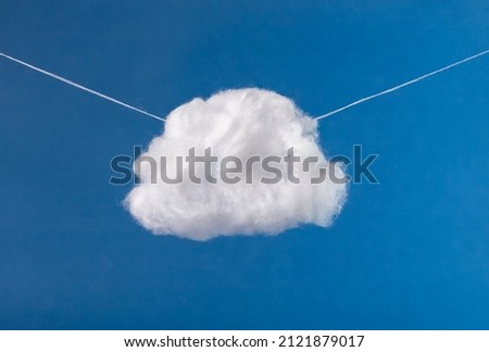 Cotton cloud hanging in blue sky on strings. Surrealism style. High quality photo Royalty-Free Stock Photo #2121879017
