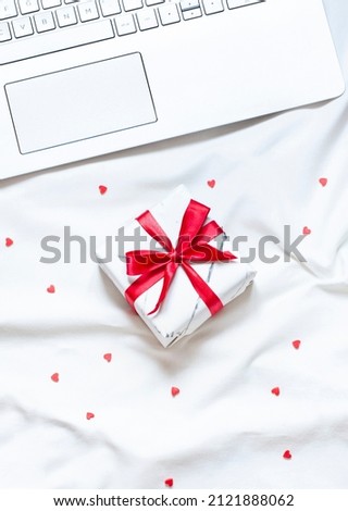 Valentine's day concept flat lay on the white blanket with a gift box and a laptop. Top view	
