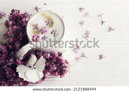 Delicious coffee with lilac petals and lilac branch on rustic white wooden background flat lay. Happy mothers day. Good morning. Hello spring. Space for text