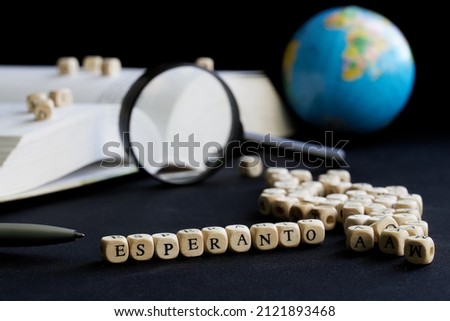 Esperanto inscription next to magnifying glass, open book, letters and small globe. Concept of learning and using the Esperanto language. Artificial language. Dark background. Selective focus Close-up