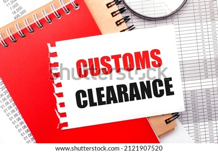 On a light background - reports, a magnifying glass, brown and red notepads, and a white notepad with the text CUSTOMS CLEARANCE. Business concept