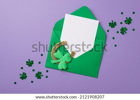 Top view photo of st patricks day decorations shamrock shaped confetti green envelope with paper card horseshoe and trefoil on isolated pastel lilac background with copyspace