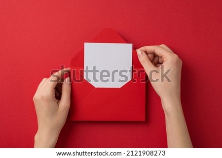 First person top view photo of valentine's day decorations female hands taking letter out of red envelope on isolated red background with blank space